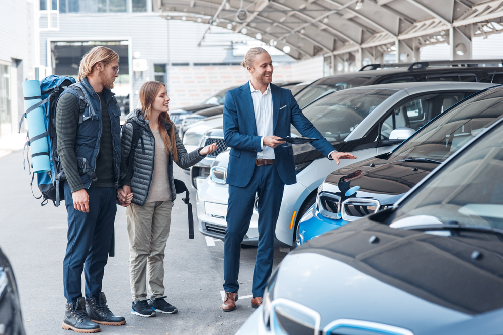 Two Happy and young adults with backpack renting their electric car.