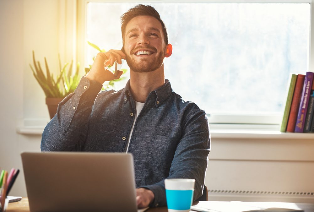 A man on the phone while using a laptop, smiling.